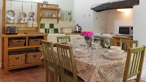 A dining area with a table set for four, surrounded by chairs, a vase with flowers, and kitchenware on shelves.