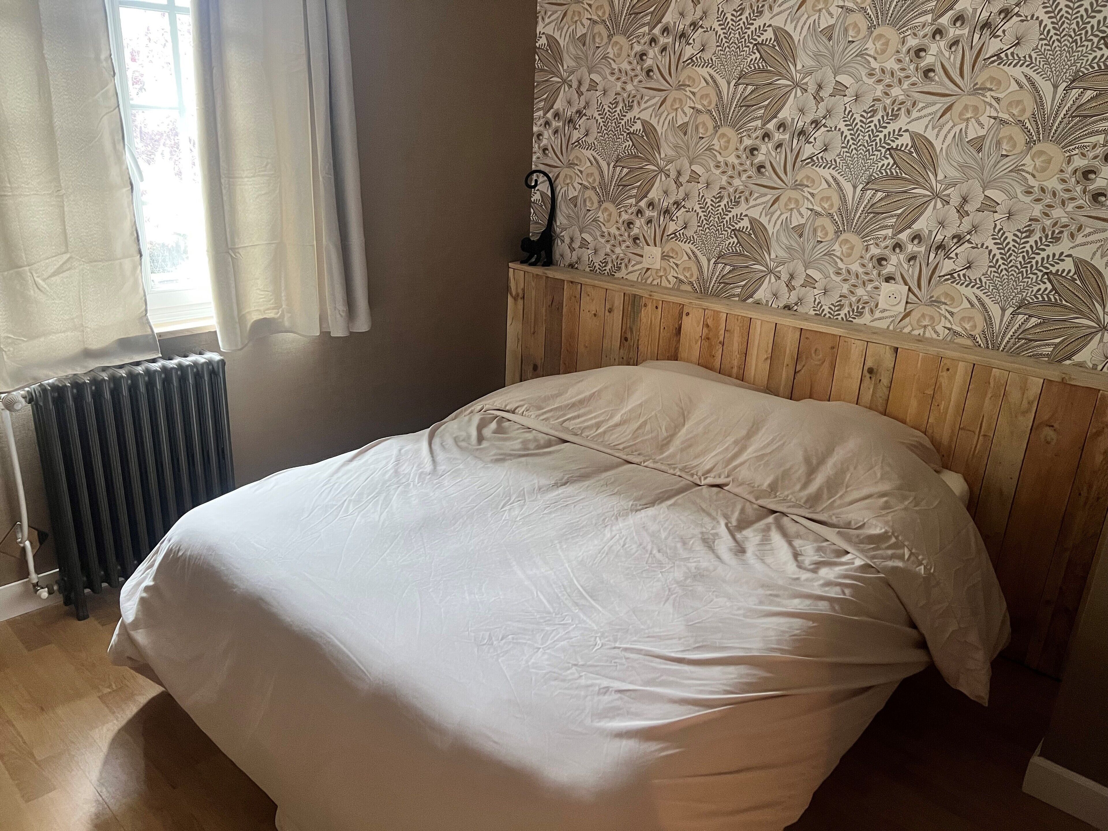 Ein Schlafzimmer mit einem hölzernen Kopfende, einem Heizkörper und einem blumigen Wandmuster.