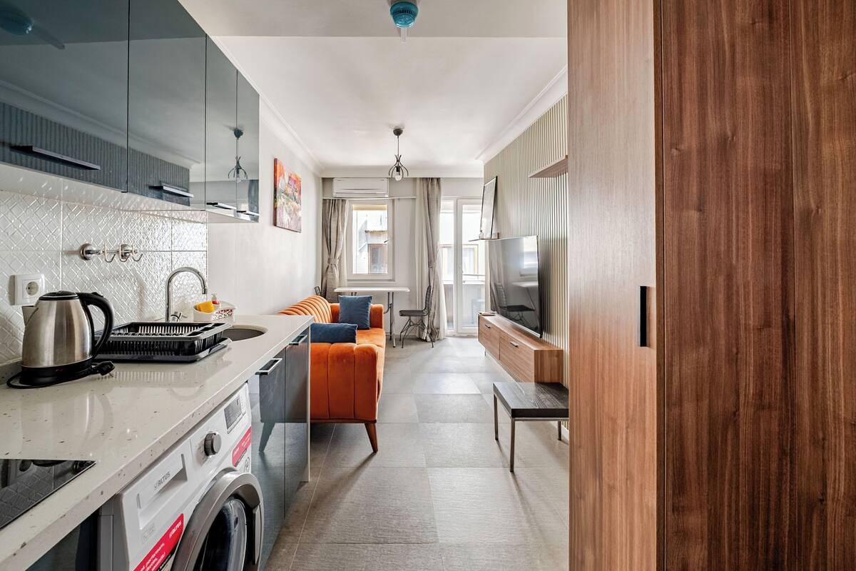 Una cocina moderna con lavadora integrada, un comedor con sofá y televisión.