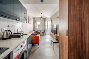 A modern kitchen with a built-in washing machine, a dining area with a sofa, and a TV.