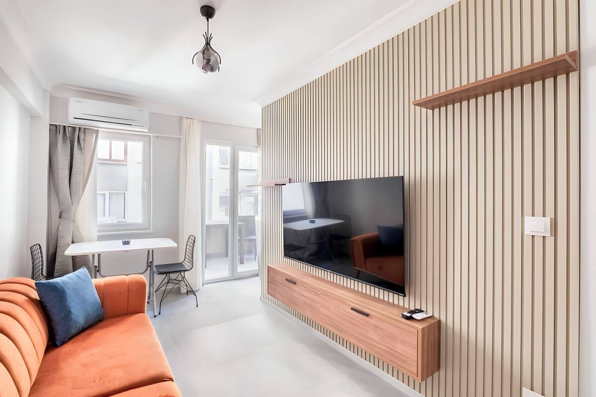 Una sala moderna con sofá, televisor y comedor con mesa y sillas.