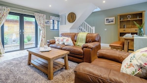 A cozy living room with a brown leather sofa, a wooden coffee table, and a staircase leading to an upper level.