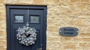 A black door with a frosted wreath, a brass handle, and a 'Bramble Cottage' sign on a stone wall.