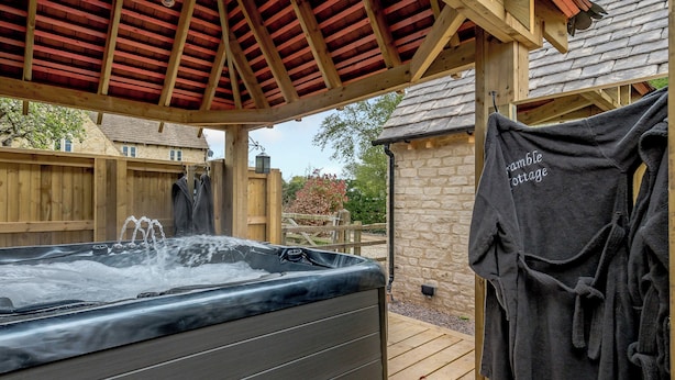 A hot tub under a wooden pergola with a stone wall and a wooden fence in the background.
