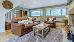 A living room with a brown leather sofa, a wooden coffee table, and a large wall clock.