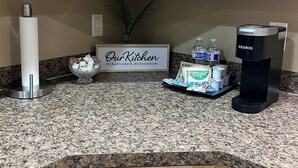 A kitchen with wooden cabinets, a granite countertop, a Keurig coffee maker, a sign that says "Our Kitchen", and a small plant. - KING bed, 2-bedroom, full kitchen, pickleball, park. Private, spacious basement. (Hooper)