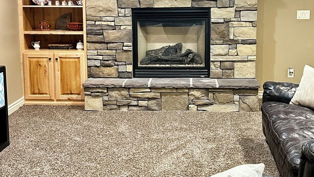 A living room with a stone fireplace, a wooden cabinet with decorative items, and a leather sofa. - KING bed, 2-bedroom, full kitchen, pickleball, park. Private, spacious basement. (Hooper)