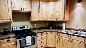 A kitchen with wooden cabinets, a stove, and a sink. - KING bed, 2-bedroom, full kitchen, pickleball, park. Private, spacious basement. (Hooper)