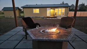 A fire pit table with chairs, a house in the background, and a wooden fence. - Private 10-Acre Retreat Near JBLM {Fast Wi-Fi} with Adjoining RV Pad (Yelm)