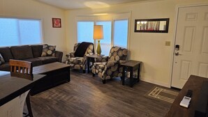 A living room with a sofa, two patterned armchairs, a coffee table, and a lamp. There is a door and a window with blinds. - Private 10-Acre Retreat Near JBLM {Fast Wi-Fi} with Adjoining RV Pad (Yelm)