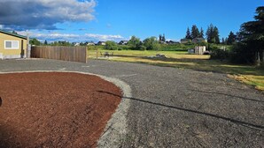 A residential area with a gravel driveway, a wooden fence, and houses in the background. - Private 10-Acre Retreat Near JBLM {Fast Wi-Fi} with Adjoining RV Pad (Yelm)