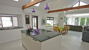 A spacious kitchen with a central island, wooden beams, and large windows offering views of the outdoors.