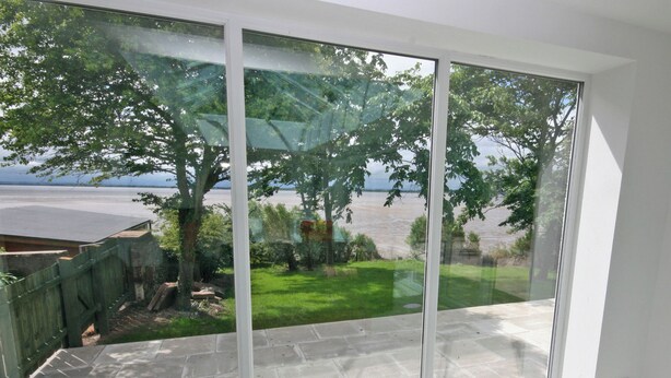 A room with a large sliding glass door leading to a patio with a view of a body of water and greenery.
