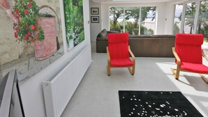 A modern living room with a large window, a radiator, a black rug, and two red chairs.
