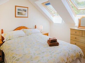 Ein Schlafzimmer mit Bett, Nachttisch, Schminktisch, einem gerahmten Bild an der Wand und Dachfenstern.