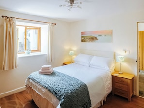 A bedroom with a bed, two bedside tables, a window with curtains, a painting on the wall, and a ceiling fan.