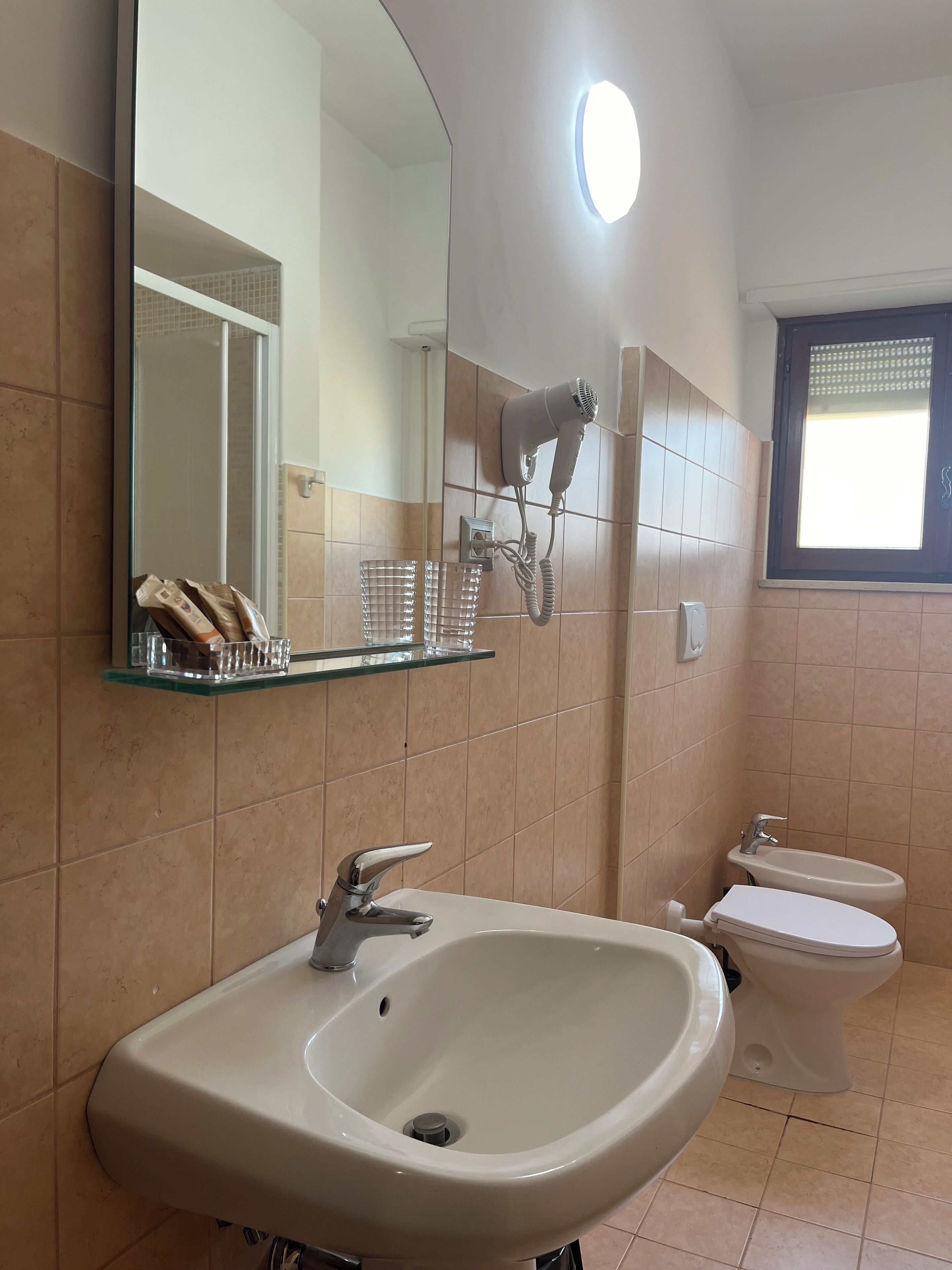 A bathroom with a white sink, a mirror, a hairdryer mounted on the wall, and a toilet.