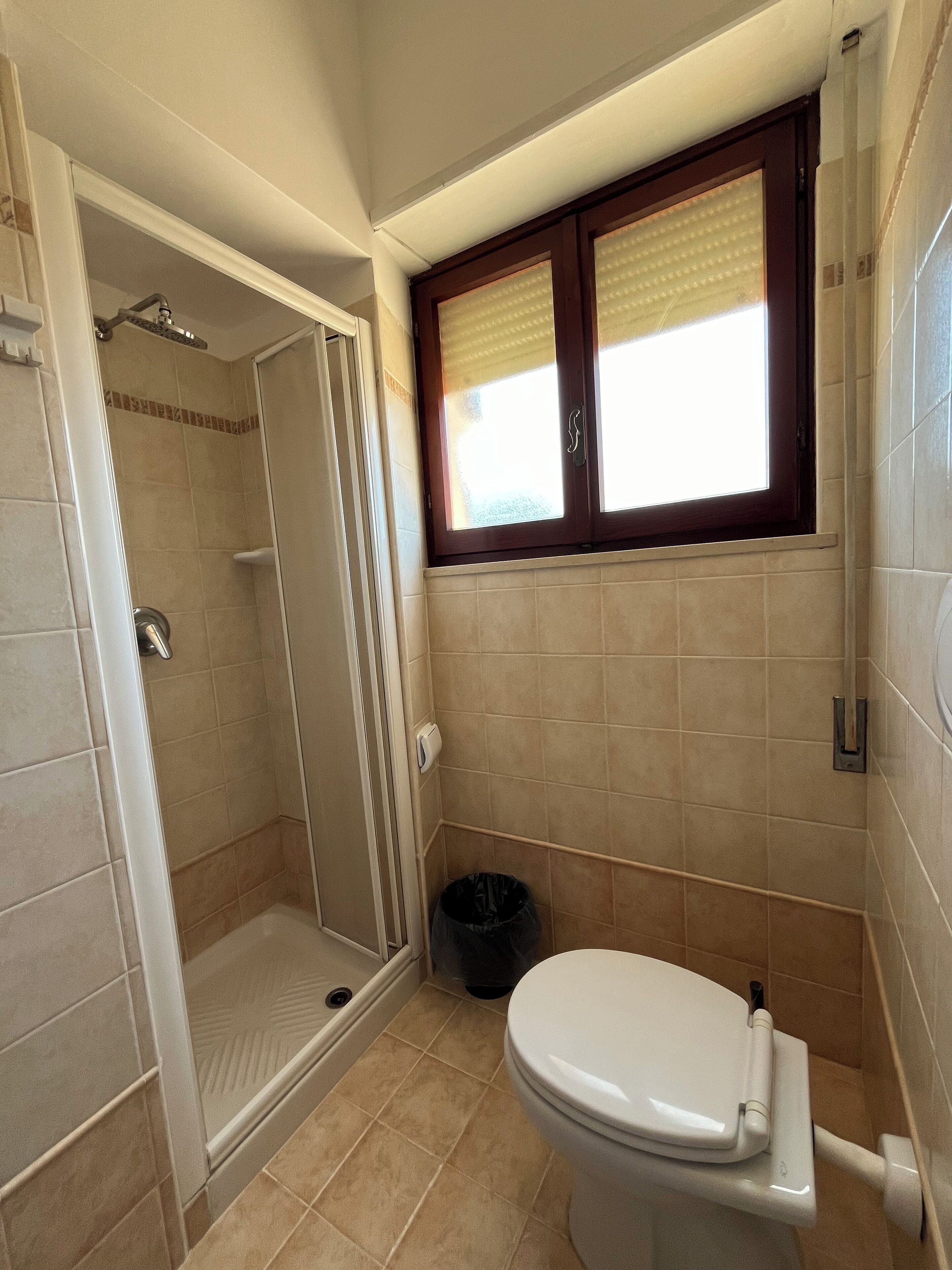 A bathroom with a shower, toilet, and a window with blinds.
