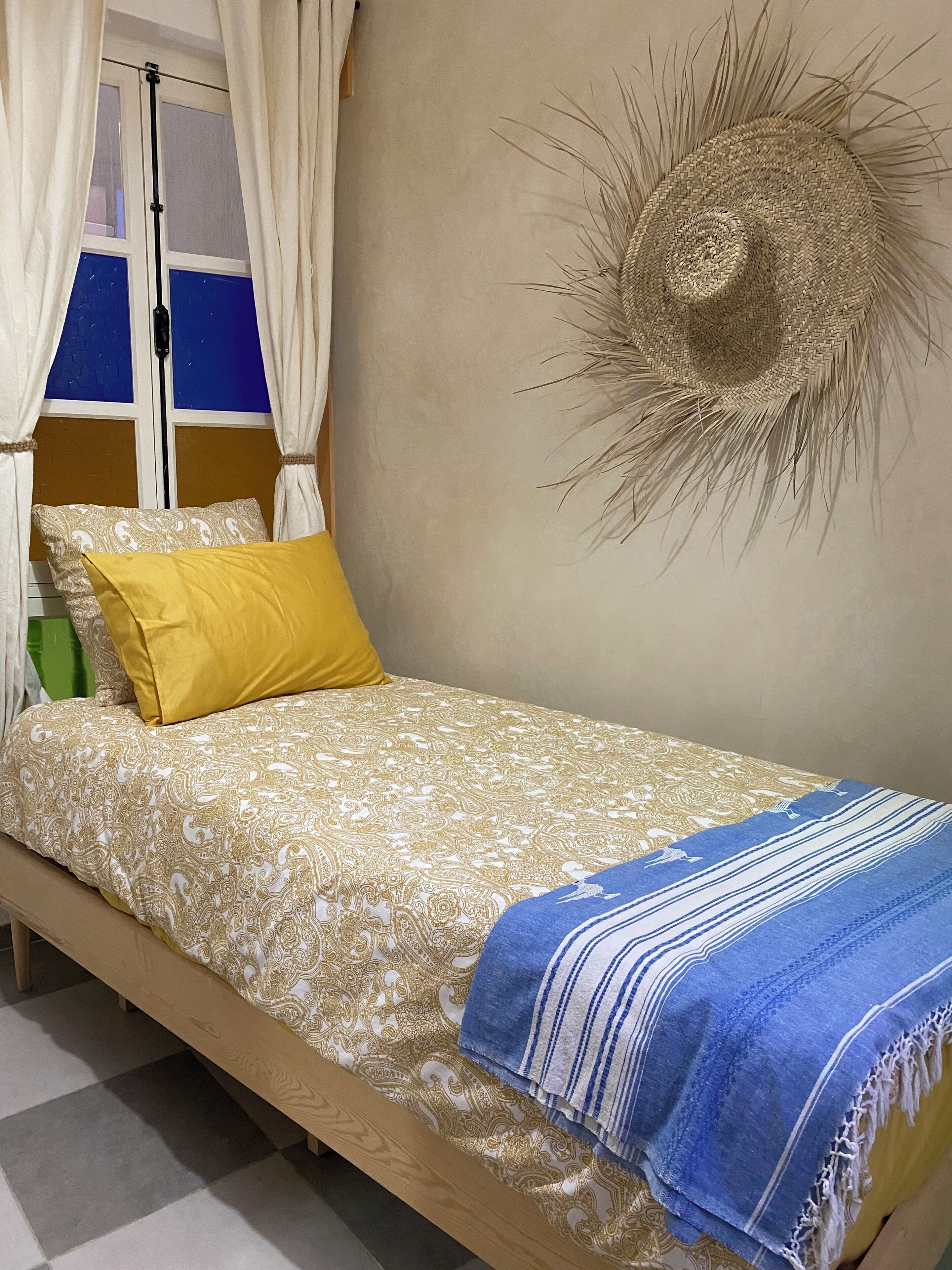 A bed with a patterned bedspread, a yellow pillow, and a blue and white striped blanket.