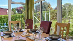 A dining table set for two with plates, bowls, glasses, and cutlery, overlooking a garden.
