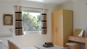 A bedroom with a bed, a wardrobe, a desk, and a window with curtains.