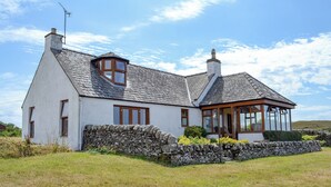 A white house with a stone wall, a tiled roof, and a glass conservatory.