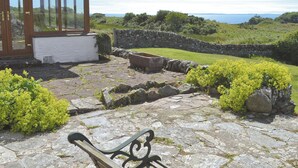 A stone patio with a bench, a stone wall, and a wooden structure with glass doors.