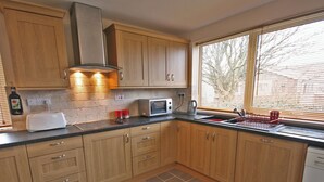 A kitchen with wooden cabinets, a microwave, a toaster, and a window with blinds. - The Five Fishers Beadnell (Beadnell)