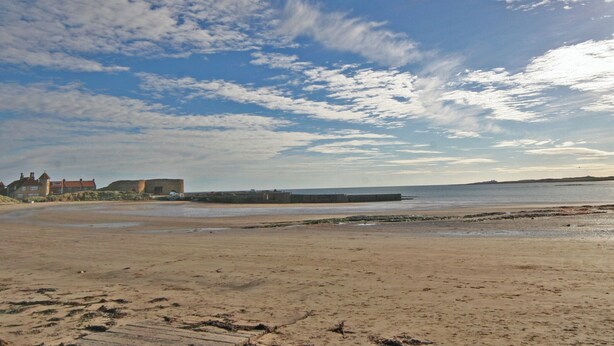 A beach with a clear sky, sandy shore, and buildings in the background. - The Five Fishers Beadnell (Beadnell)