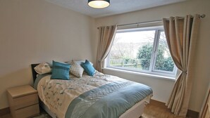 A bedroom with a bed, a nightstand, a window with curtains, and a view of the outside. - The Five Fishers Beadnell (Beadnell)