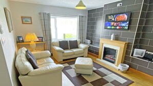 A living room with a sofa, ottoman, fireplace, television, and a checkered rug. - The Five Fishers Beadnell (Beadnell)