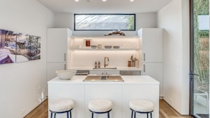 Une cuisine moderne dotée d’un îlot central, de meubles blancs et d’une grande fenêtre au-dessus de l’évier.