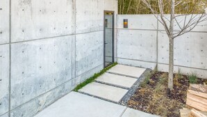 Un bâtiment moderne avec une façade en béton, une porte en verre et un petit arbre au premier plan.