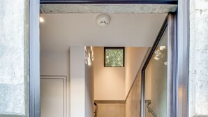 Un escalier moderne avec des marches en bois et une rampe en verre, menant à une porte surmontée d’une petite fenêtre.