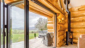 L’intérieur d’une cabane en rondins, avec une porte vitrée donnant sur un patio, une cheminée et un espace salon extérieur.