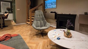 Un salon moderne avec un fauteuil gris, une table basse ronde en marbre et un téléviseur fixé au mur.