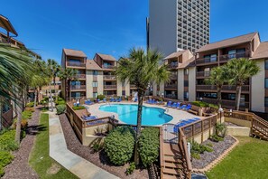 Un hotel con piscina centrale circondata da lettini e palme.