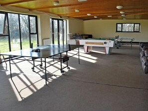 Une pièce équipée d’une table de ping-pong, d’une table de billard et d’une table de jeu de fléchettes. De grandes fenêtres laissent entrer la lumière naturelle et offrent une vue sur l’extérieur.
