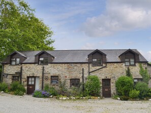 A stone building with multiple windows and doors, surrounded by gravel and greenery.
