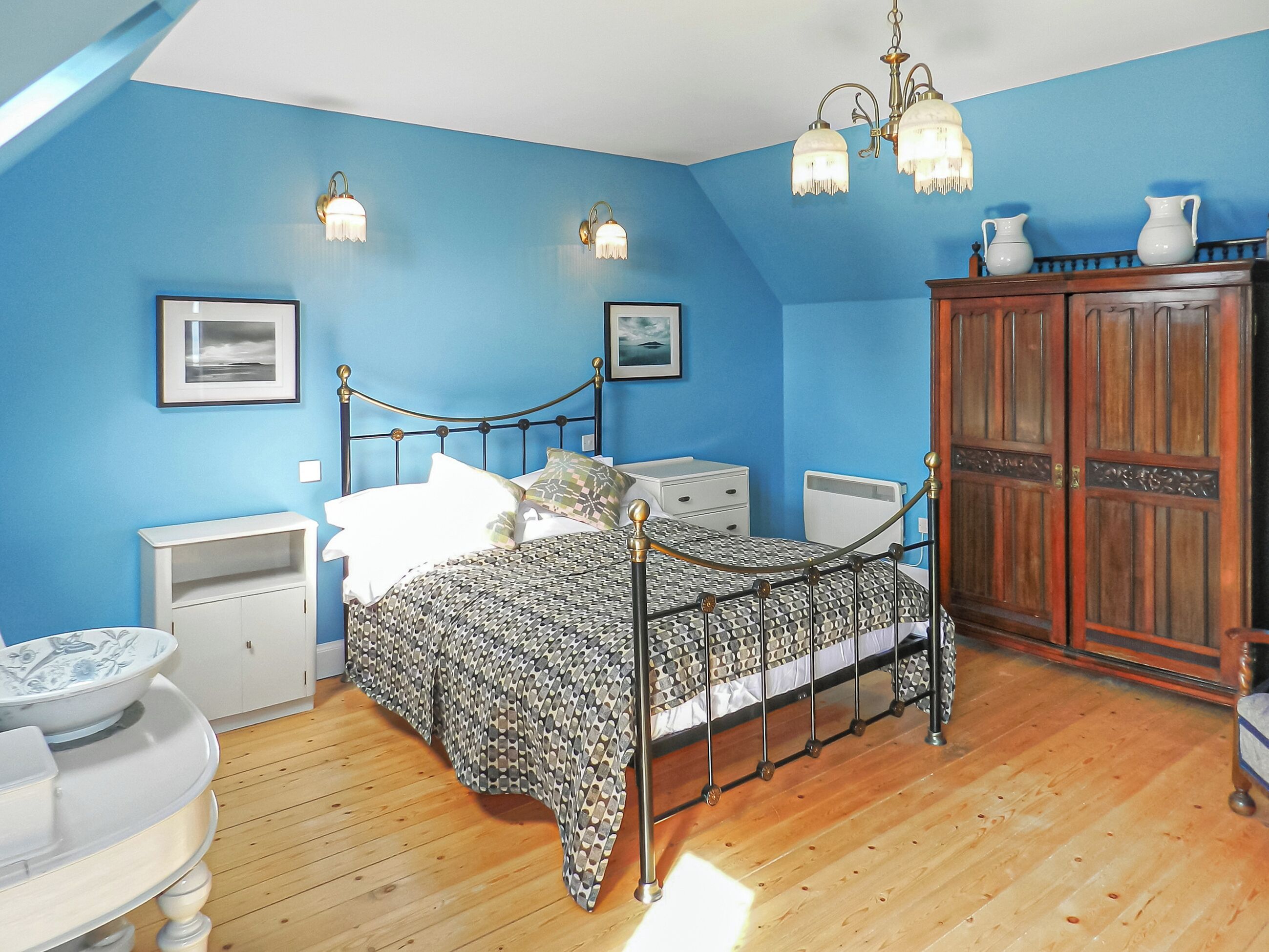 Un dormitorio con cama, mesitas de noche, armario y candelabro.