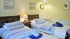Een hotelkamer met twee bedden, een nachtkastje met een lamp, een spiegel, een wastafel en kunstwerken in lijsten aan de muur.