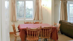 A dining room with a table set for six, surrounded by wooden chairs, a sofa, and a window with curtains.