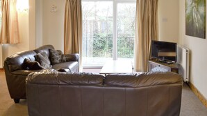 A living room with a brown leather sofa, a television on a stand, and a large window with curtains.