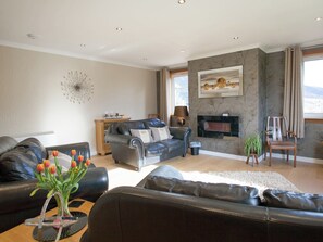 Una sala de estar con chimenea, un sofá, una mesa de centro con un jarrón de tulipanes y un televisor montado en la pared.
