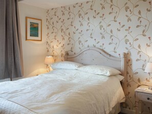 Un dormitorio con cama, mesita de noche, lámpara y papel tapiz con motivos florales.