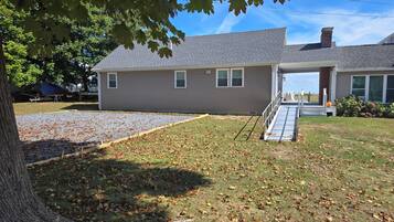 A two-story house with a covered porch, a gravel driveway, and a lawn with scattered leaves.