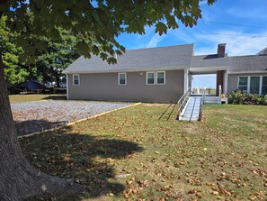 A two-story house with a covered porch, a gravel driveway, and a lawn with scattered leaves.