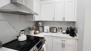 Une cuisine moderne avec des meubles blancs, une cuisinière noire, une machine à café et un grille-pain.