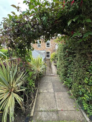 A narrow stone pathway leading to a stone building with multiple windows and a sloped roof.