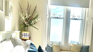 A bedroom with a large bed, multiple pillows, a vase with flowers, and a window with starfish decorations. - Stylish Elie Beach Retreat sea-view and Sunny deck (Elie and Earlsferry)